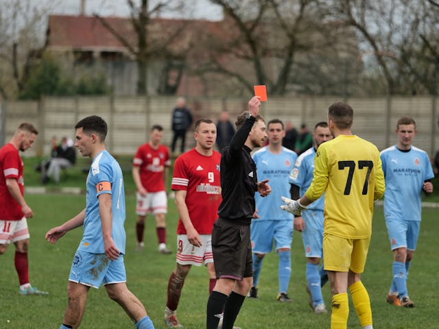A photo of a referee sending a player off during a match. The player being sent off is protesting the decision to the referee.