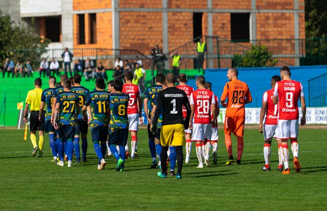A photo of a referee leading two football teams onto the field ahead of kick off.